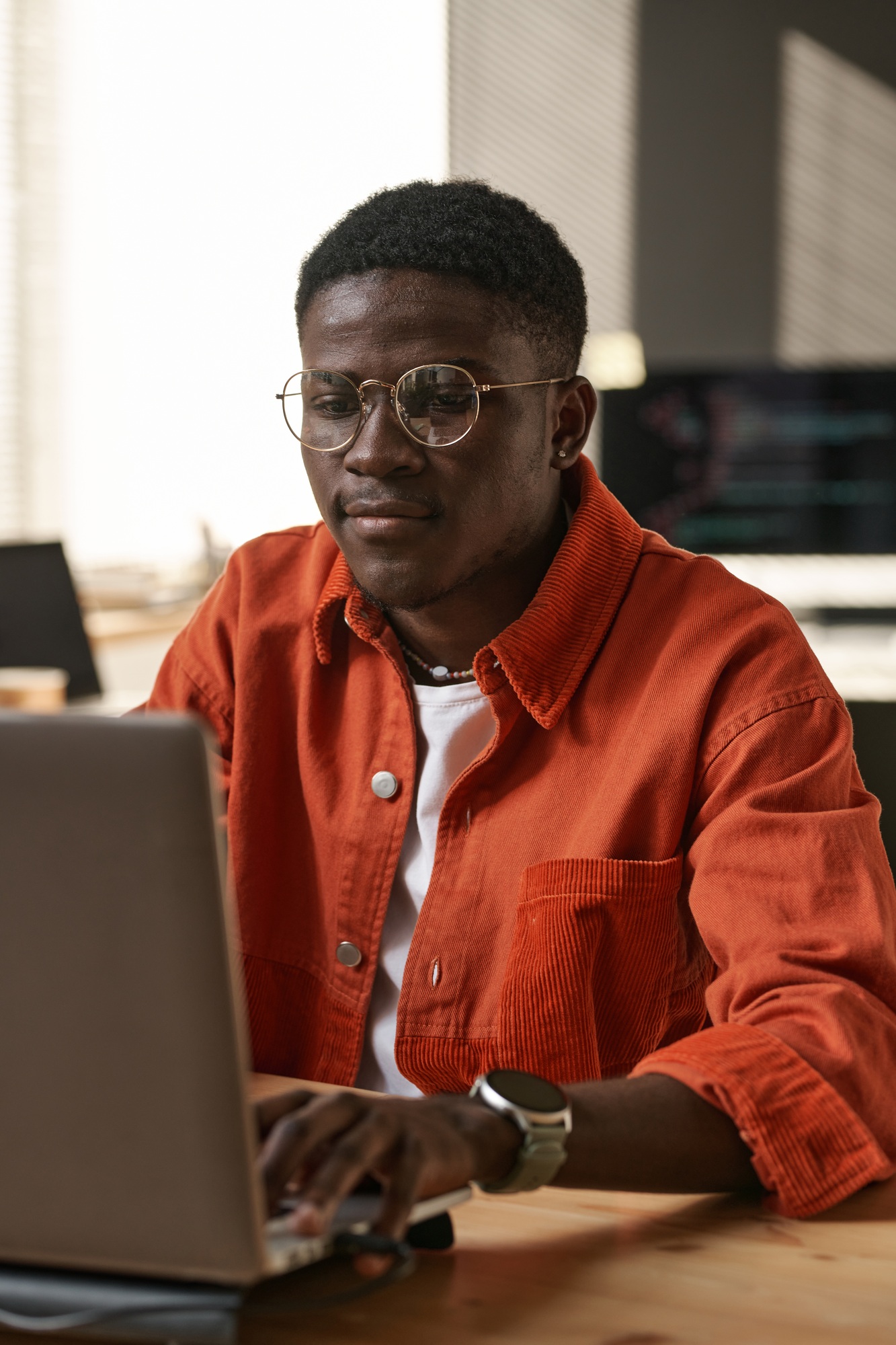 Serious young IT support engineer sitting by workplace in front of laptop